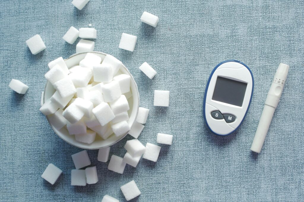 Diabetes e Alimentação: Como Comer Bem, Controlar a Glicemia e Nunca Mais se Sentir Preso a Uma Dieta Sem Graça Overhead shot of a glucometer and sugar cubes representing diabetes management and sugar intake.