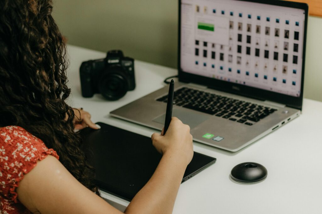 Trabalho Remoto Sem Inglês Fluente: É Possível Começar em 2026? Woman using pen tablet with laptop and camera in creative workspace.