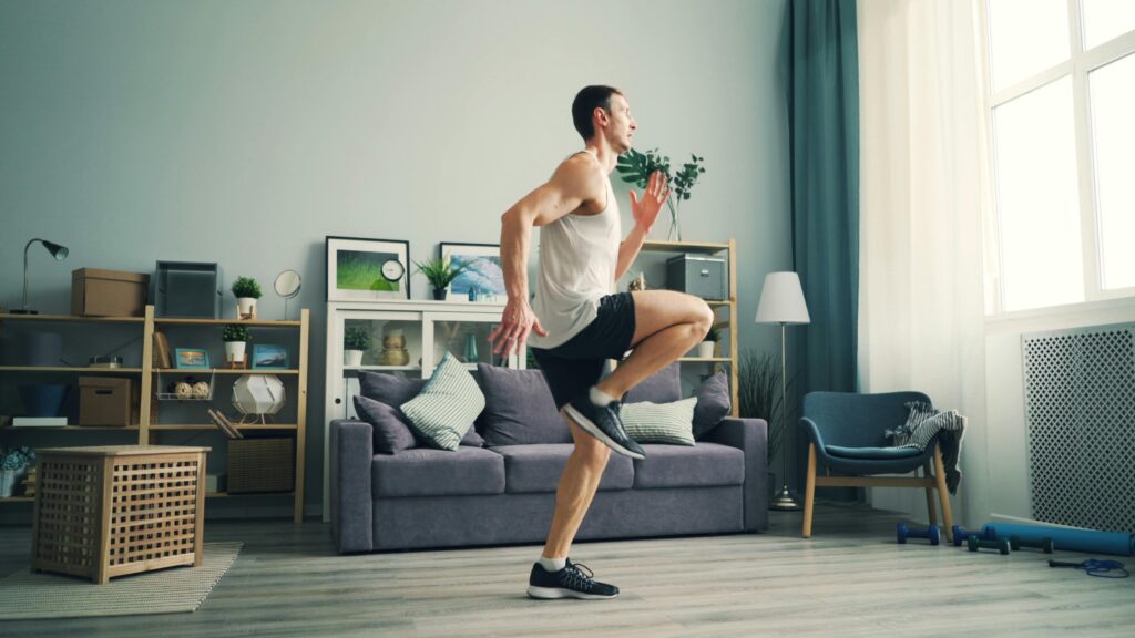 Treino Funcional em Casa: Como Transformar Seu Corpo Sem Academia, Equipamentos ou Mensalidade A man in sportswear exercising indoors with a modern living room background.