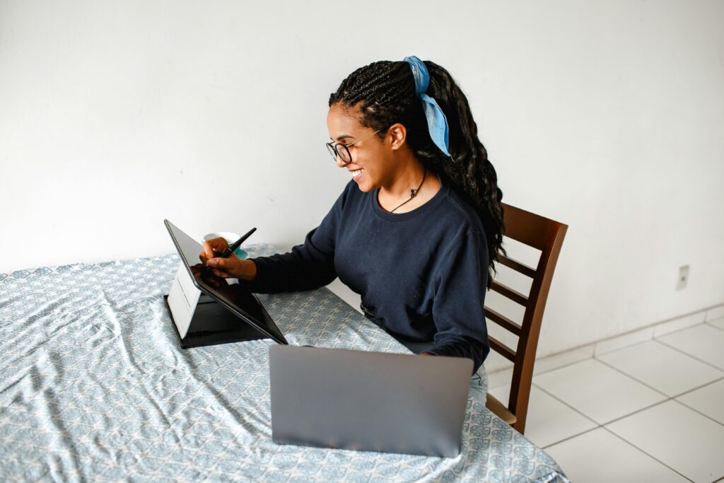 Produtividade Sem Culpa: Como Trabalhar em Casa de Verdade (Sem Ser Escravo do Hustle) Woman working remotely using a tablet and laptop at home. Ideal for tech or remote work themes.
