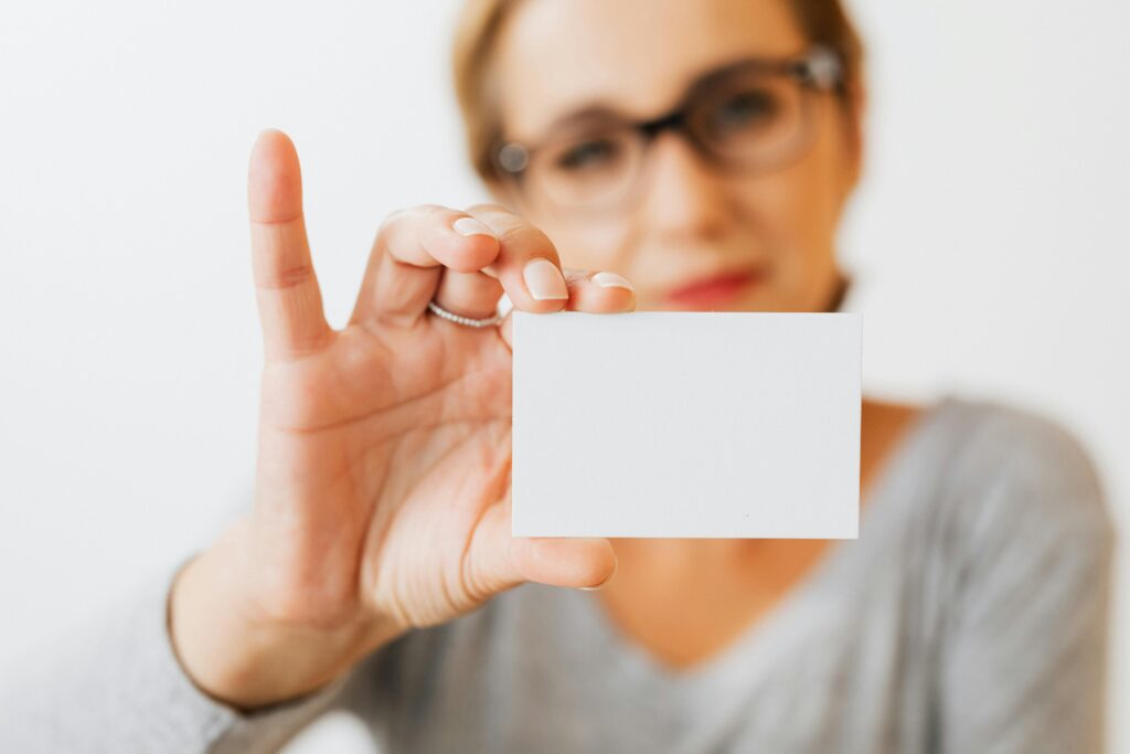 Gestor de Tráfego: Como Conseguir Clientes Todos os Dias Sem Precisar de Acesso à BM ou ao Pixel Close-up of a woman holding a blank business card with a blurred background for copyspace.