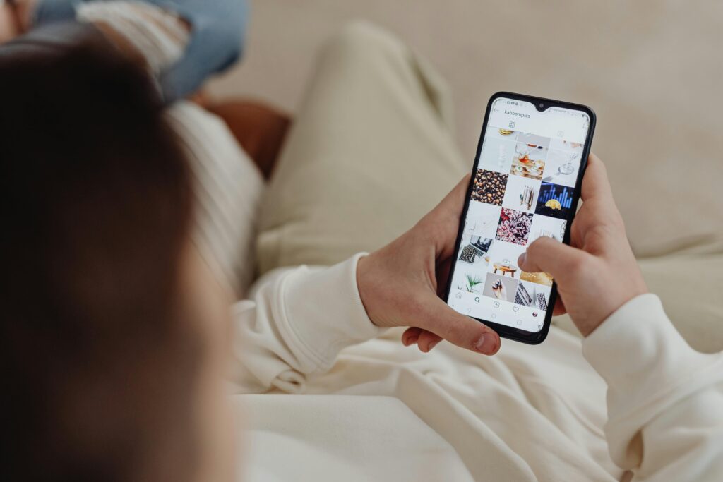 Você Posta Todo Dia e Não Vende Nada? Descubra o Que Está Errado (e Como Corrigir) Person using smartphone to browse Instagram indoors, showing social media engagement.