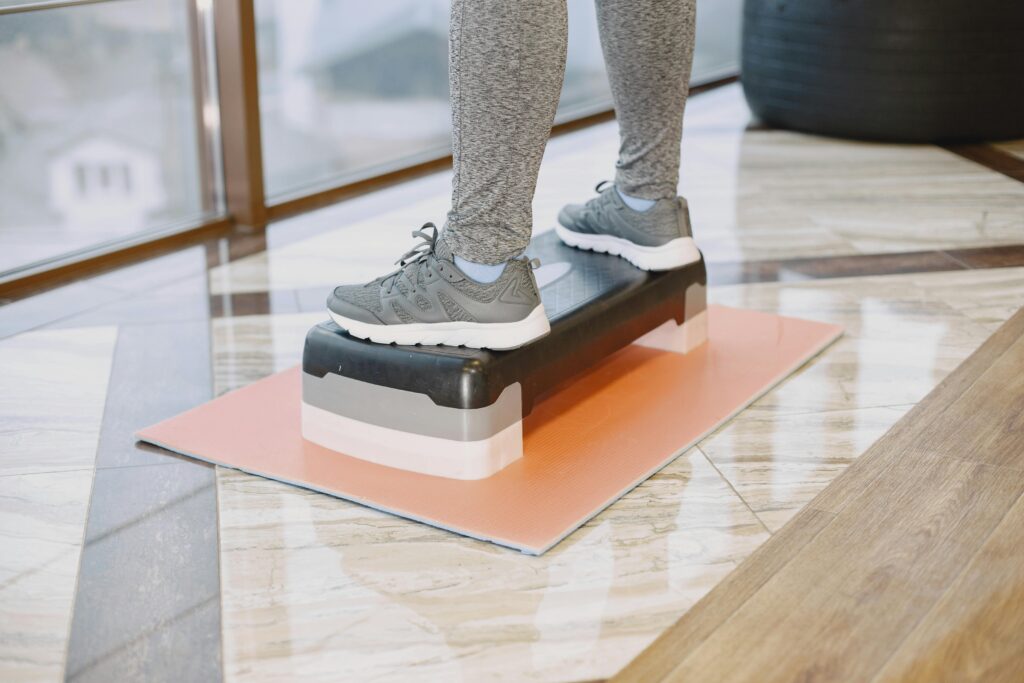 Treino com Step: A Modalidade Que Queima Gordura Até 5x Mais Rápido (e Você Pode Fazer em Casa) A person exercising indoors using a step platform for a workout routine.