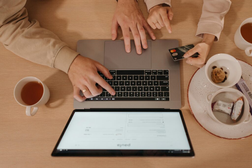 Tráfego Pago: A Profissão Digital Que Pode Te Pagar Entre R$500 e R$20.000 Por Mês (e Como Aprender do Zero) Two people using a laptop for online shopping with a credit card, seen from above.