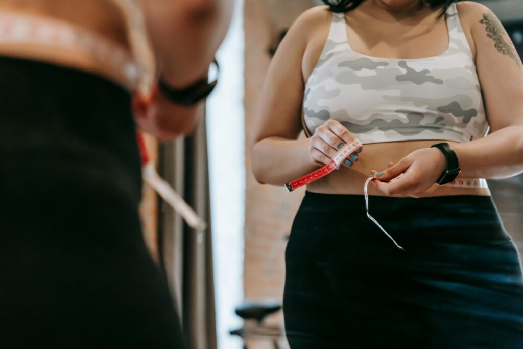 21 Dias Para um Corpo Diferente: O Desafio que Já Transformou Mais de 45 Mil Mulheres Low angle of crop faceless overweight female in activewear reflecting in mirror in sports club