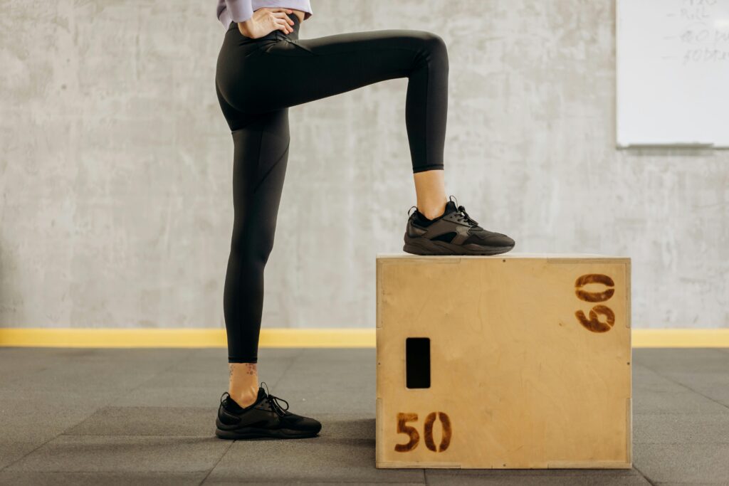 Treino com Step: A Modalidade Que Queima Gordura Até 5x Mais Rápido (e Você Pode Fazer em Casa) Female athlete performing workout in gym with wooden step box, showcasing fitness and balance.