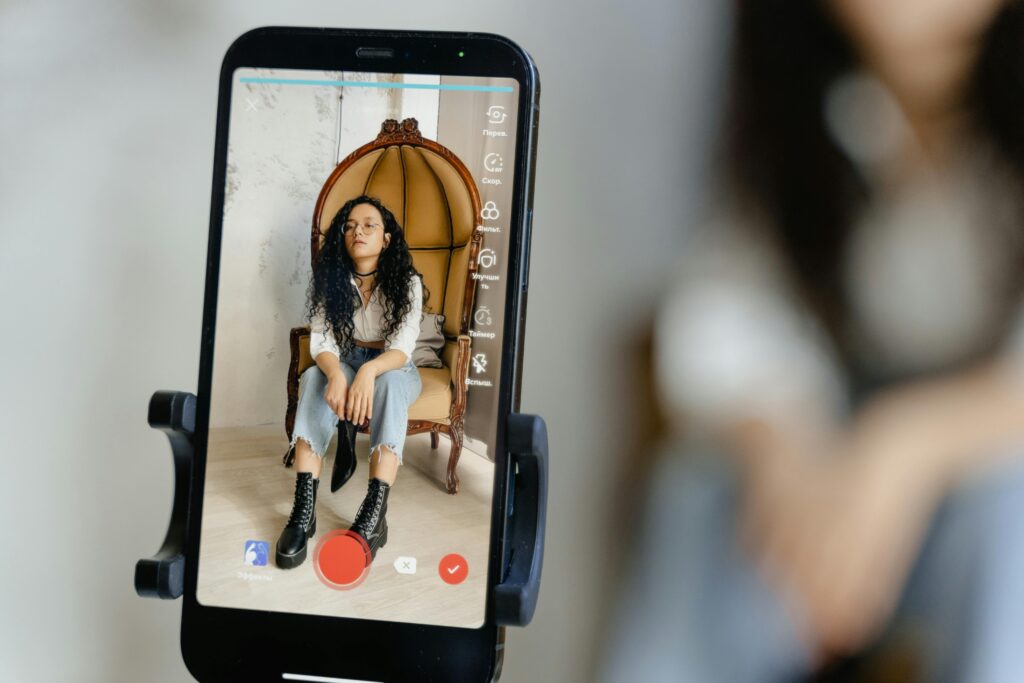 Como Criar Imagens Profissionais com IA: A Habilidade Que Está Criando uma Nova Categoria de Profissionais Criativos A woman sits in a chair recording a video on her smartphone, showcasing modern vlogging techniques.