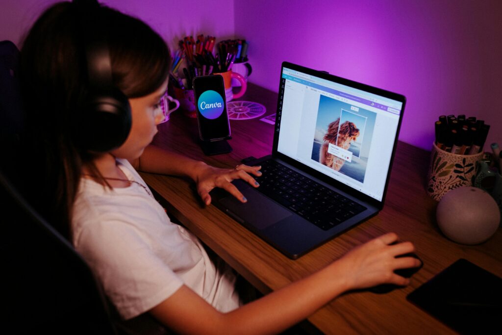 Habilidades Mais Valorizadas no Trabalho Remoto em 2026 Young girl using a laptop with headphones under purple lighting, focused on photo editing.