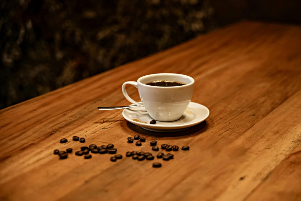 O Que Especialistas Dizem Sobre Beber Café em Jejum Toda Manhã A cozy scene of a coffee cup and beans on a wooden table in a café.