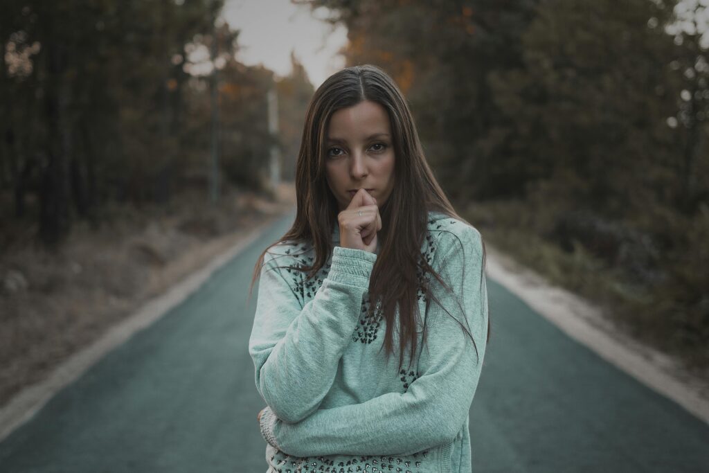 Pensive woman standing on a quiet forest road, lost in thought. Outdoor portrait.