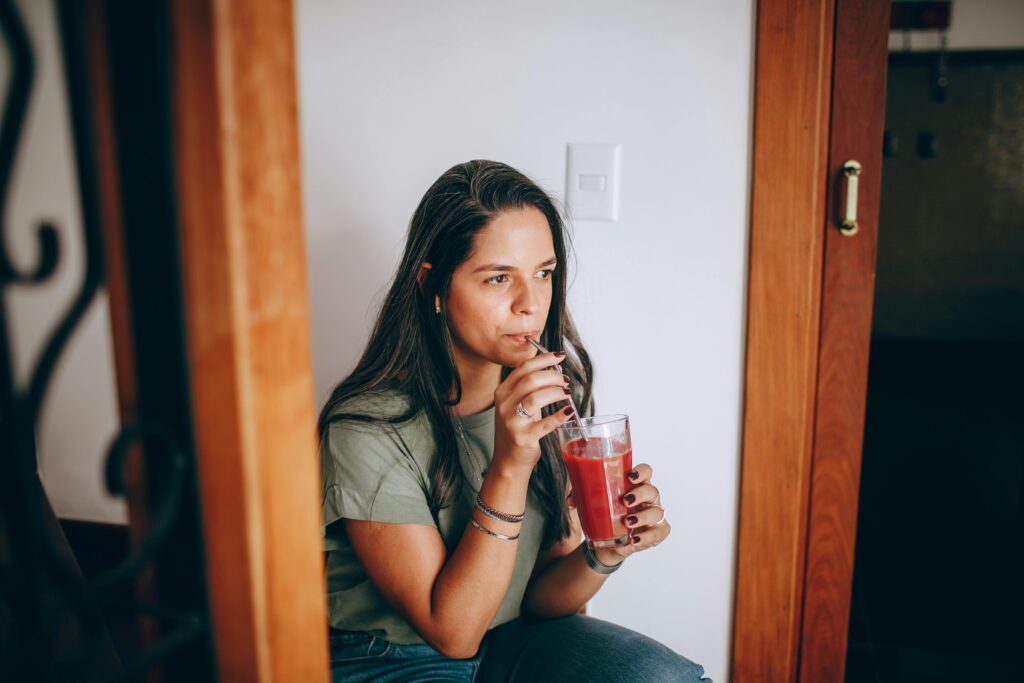 Como Reduzir a Inflamação do Corpo Com Alimentação (Guia Prático) A woman enjoying a refreshing drink indoors, captured in a relaxed moment.