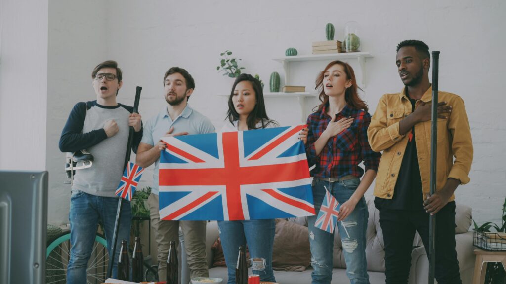 Inglês Para Quem Não Tem Tempo: Como Aprender de Verdade na Rotina do Dia a Dia A diverse group of adults perform an anthem indoors, displaying the UK flag passionately.