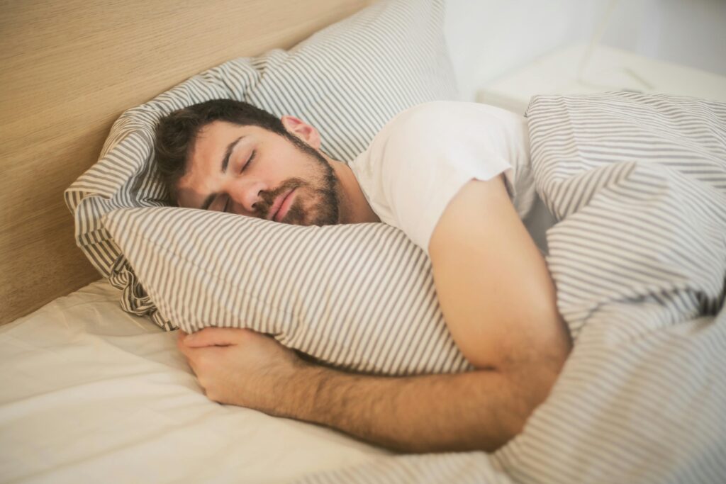 Como Melhorar a Qualidade do Sono Sem Remédios Man sleeping peacefully on striped bedding, embracing relaxation and comfort.