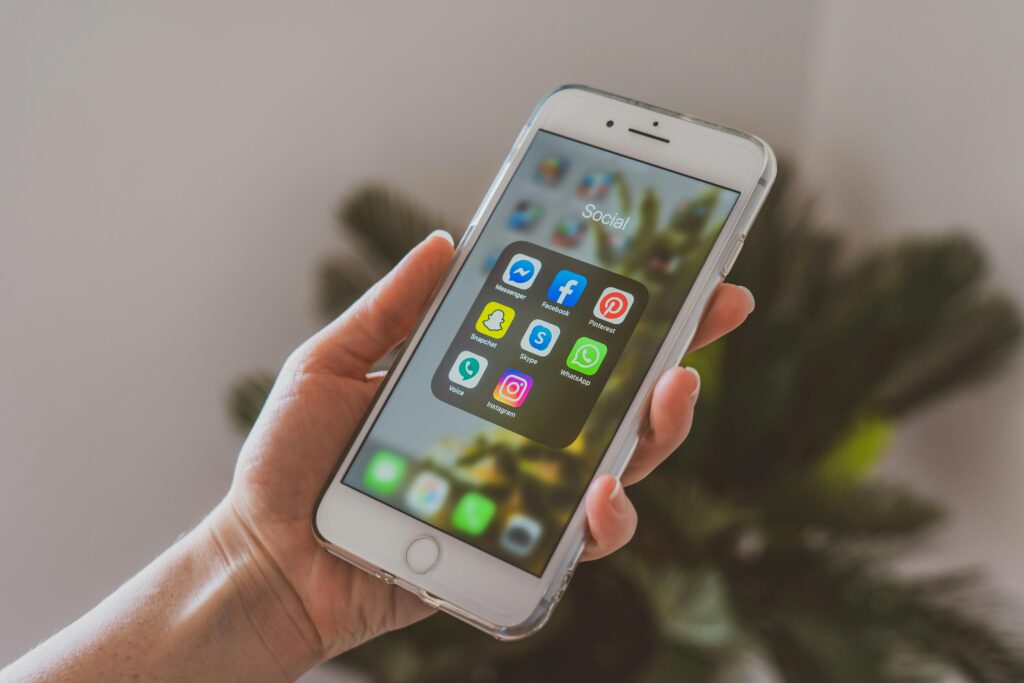 Atendimento Remoto via WhatsApp: Como Conseguir Clientes e Trabalhar de Casa Close-up of a hand holding a smartphone displaying popular social media apps.