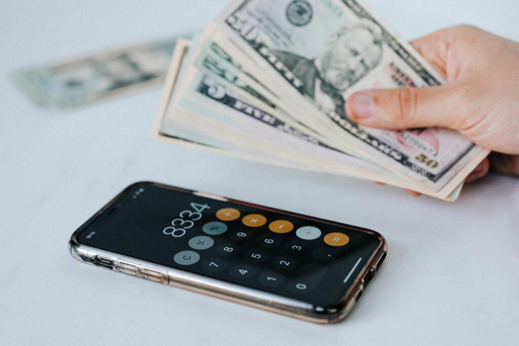 Como Ganhar Dinheiro em Dólar pela Internet Sem Sair do Brasil Calculator application on mobile phone screen on white surface near crop anonymous person holding pile of dollars