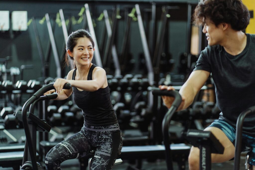 Exercício Físico e Saúde Mental: A Conexão Que a Ciência Comprova Happy Asian couple working out on elliptical trainers in a gym.
