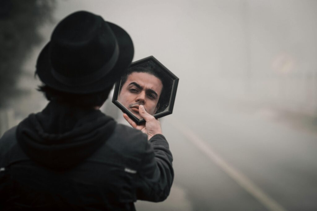 A mysterious man in a black hat reflects in a mirror on a foggy road.
