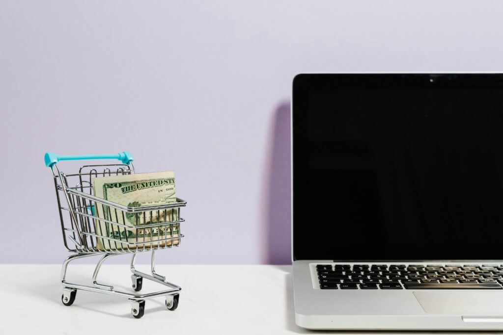 Inglês Profissional: A Habilidade que Pode te Fazer Ganhar em Dólar Shopping cart with money next to a laptop symbolizing online shopping and e-commerce.