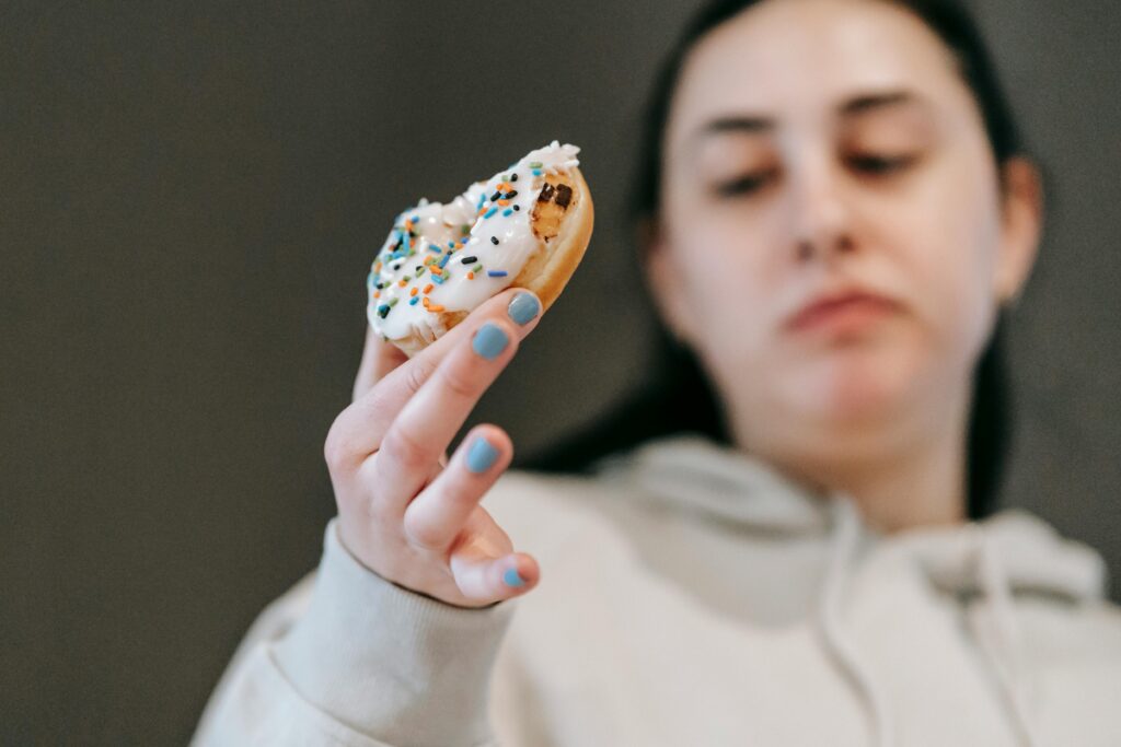 Glúten: Quem Realmente Precisa Evitar e Quem Está Exagerando Crop emotionless female in casual wear chewing tasty doughnut glazed with vanilla icing in light room