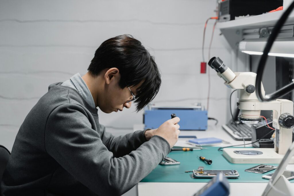 Curso de Conserto de Celular: Aprenda uma Profissão que Nunca Falta Cliente Professional technician repairing mobile devices using a microscope in a lab.