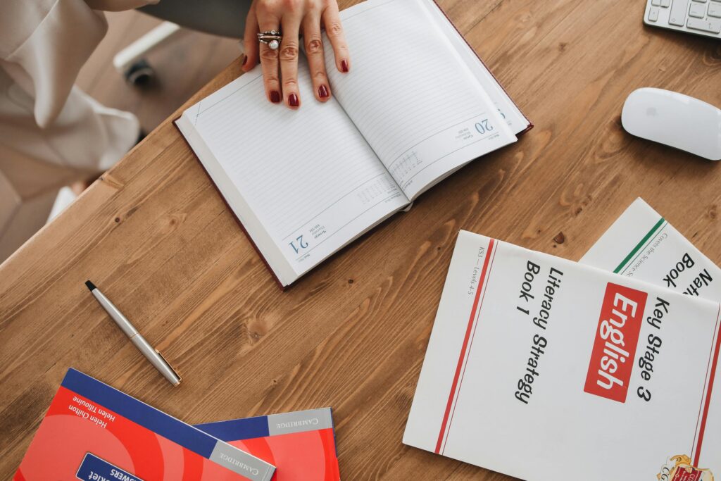 Inglês para Trabalho e Entrevistas: Pare de Perder Oportunidades por Causa do Idioma High angle view of a student studying with English literacy books and an open diary for note-taking.