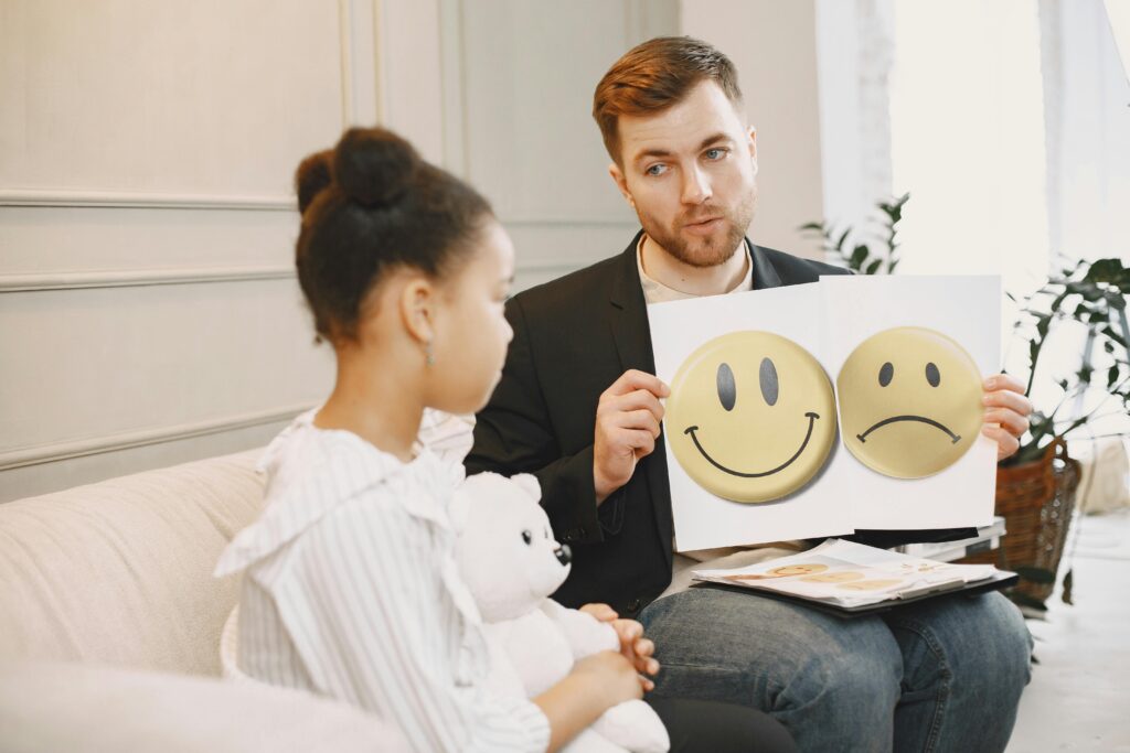 Como Desenvolver Inteligência Emocional na Prática do Dia a Dia A therapist uses emotion cards to help a child express feelings during a counseling session.