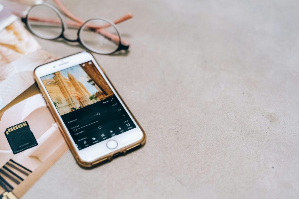 Ganhe Dinheiro Fazendo Vídeos Pelo Celular: Como Faturar até R$10 Mil por Mês Smartphone displaying a photo editing app, next to a memory card and glasses on a table.