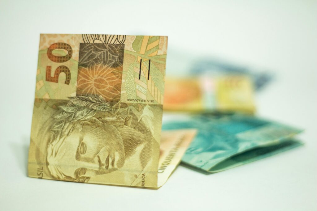 Como Fazer Seu Dinheiro Trabalhar Enquanto Você Dorme Brazilian Real banknotes in focus with 50 denomination displayed prominently.
