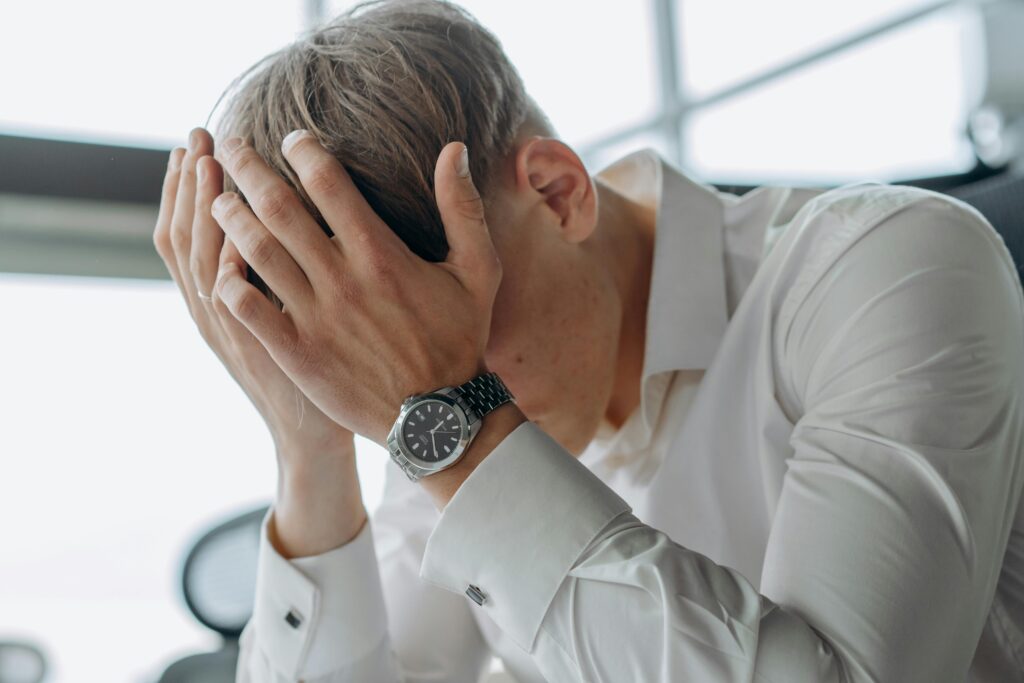 O Segredo das Pessoas Que Sempre Parecem Calmas Sob Pressão A business professional showing stress and fatigue with head in hands.