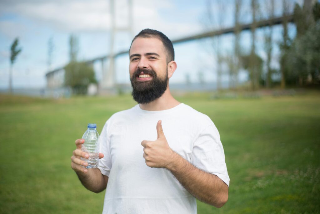 Longevidade: Os Hábitos de Quem Vive Mais de 90 Anos Com Saúde Cheerful man with a beard giving thumbs up while holding a water bottle in a park setting in Portugal.