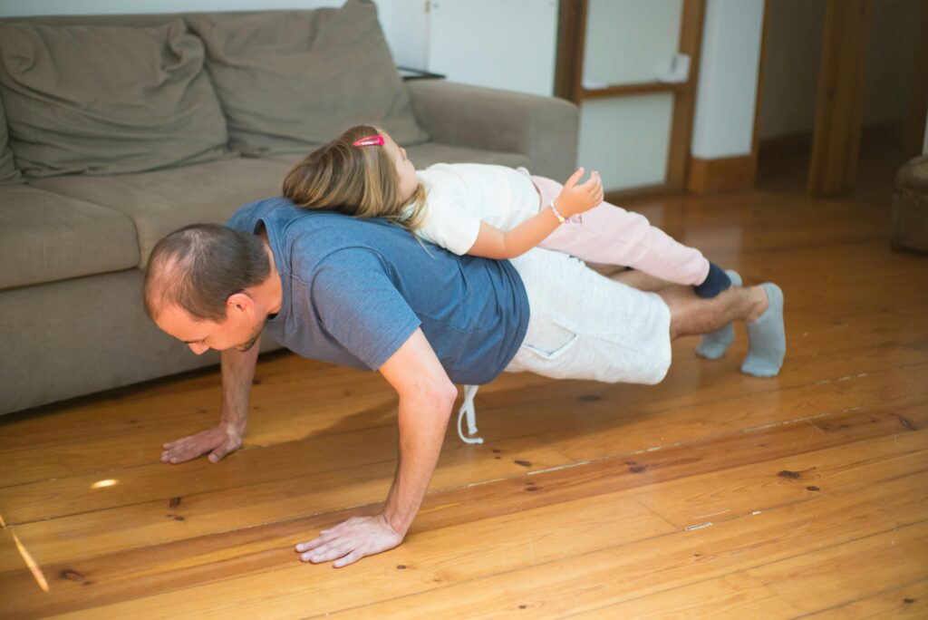 Father doing push-ups with daughter on his back in a cozy home setting.