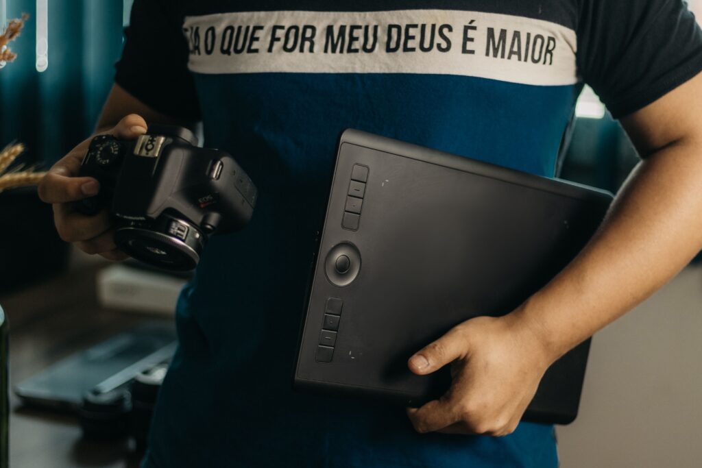 A photographer holds a Canon camera and a Wacom graphics tablet, ready for editing work.