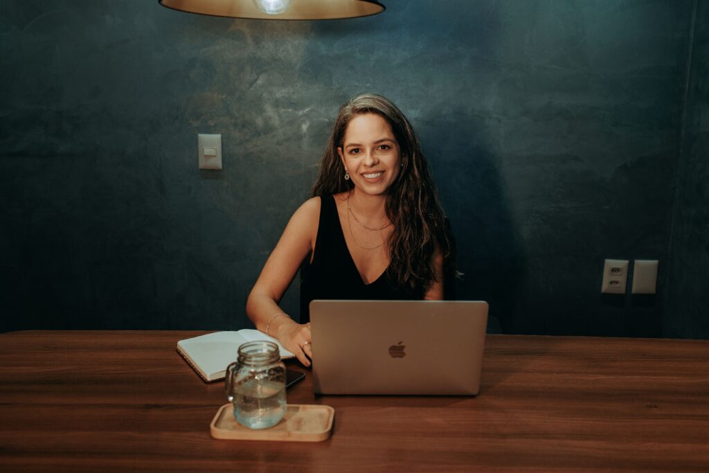 Woman working on a laptop in a cozy home office, smiling at the camera.