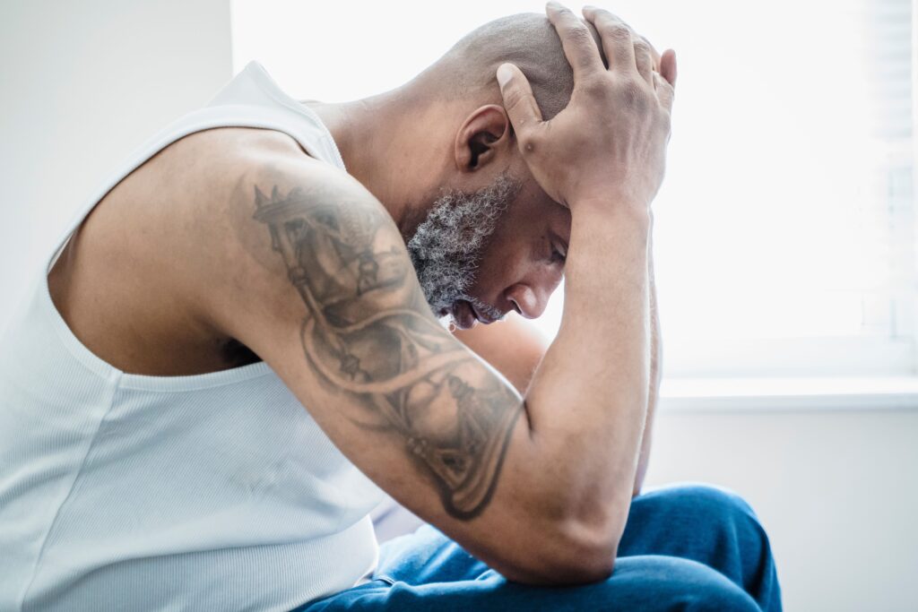 Side view of a thoughtful bald man with an arm tattoo, sitting indoors.